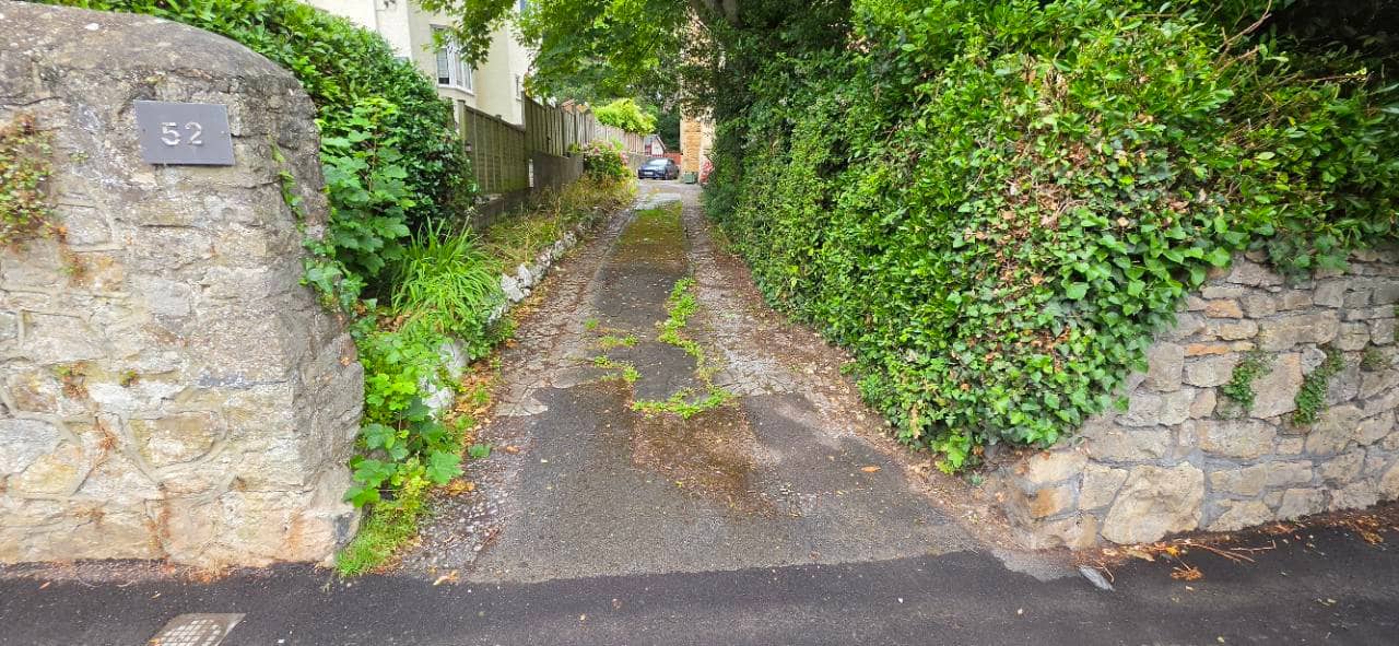 Before photo of a worn and overgrown driveway entrance in Weston-super-Mare before Canberra resin bound surfacing