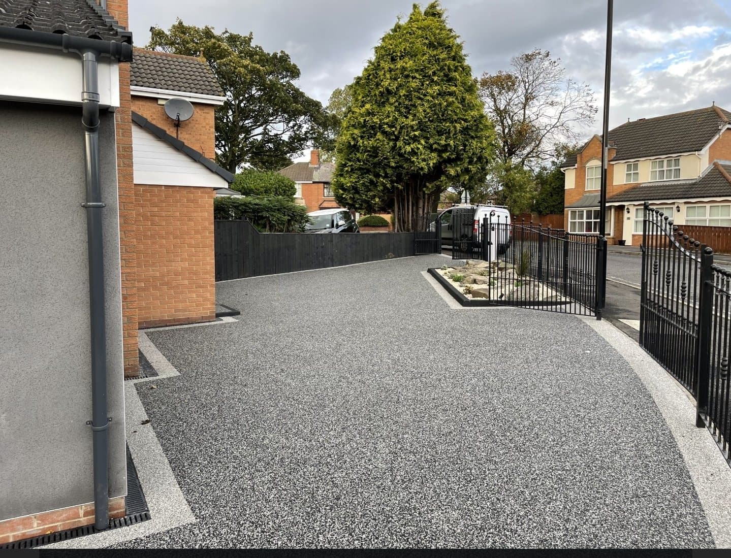 Grey resin driveway with railings and rockery border